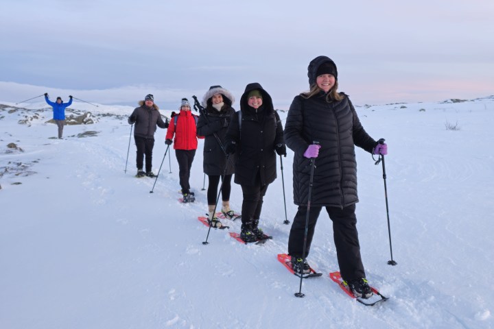 Group of people snowshoeing in a line on a snowy landscape.